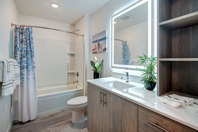 Modern apartment bathroom with quartz vanity, illuminated mirror, and soaking tub at Admiral Station Apartments.