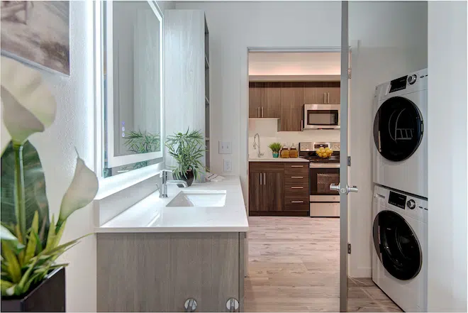 Apartment bathroom with in-home washer and dryer leading into a modern kitchen at Admiral Station Apartments.