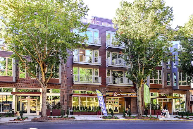 Front exterior of Admiral Station Apartments in West Seattle with modern balconies, street-level retail, and mature trees.