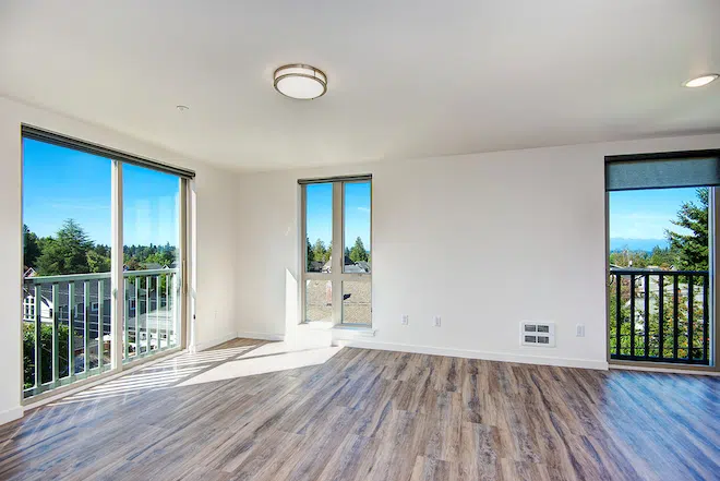 Open-concept apartment living room with balcony access and large windows overlooking West Seattle.